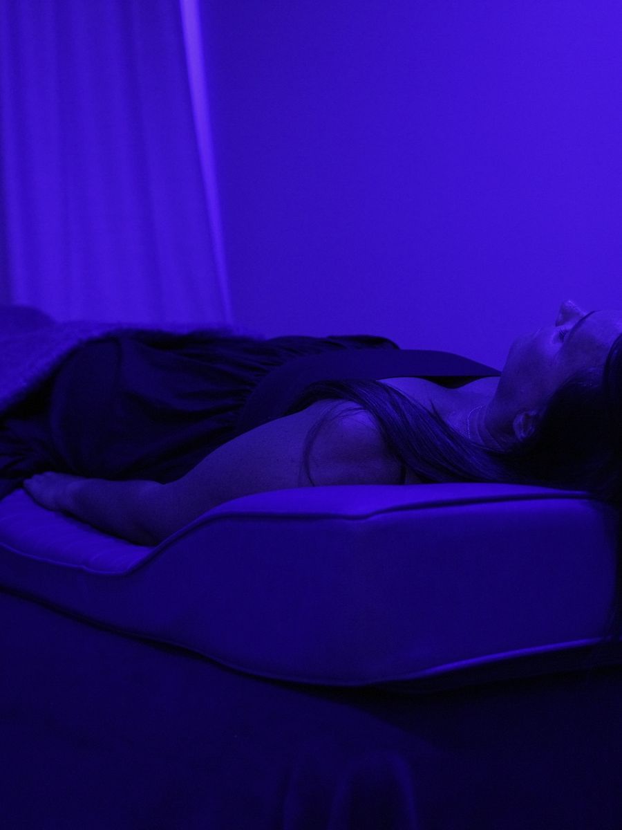 A person lying on the PEMF bed at Renew under deep blue light