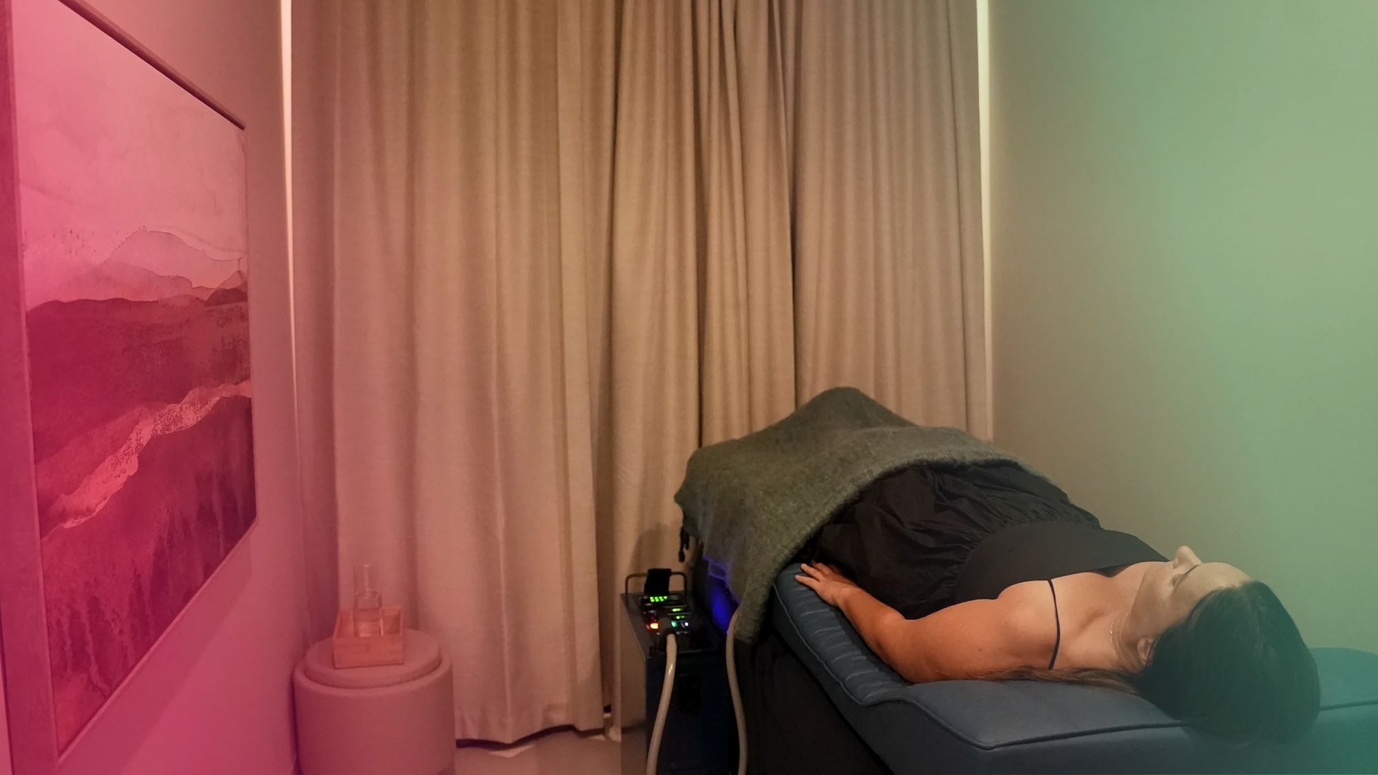 Someone lying under a blanket on the PEMF bed at Renew, with the controller beside them
