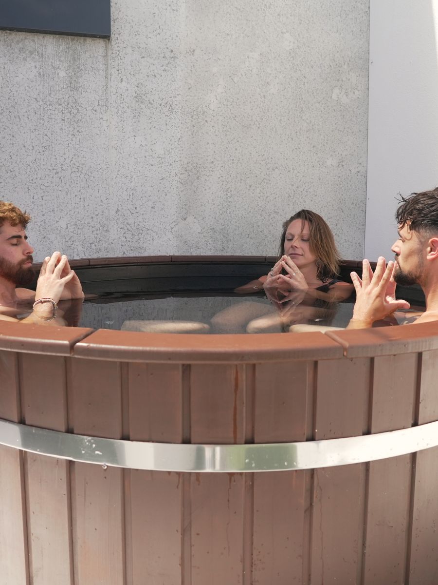 Three people in the wooden plunge tub on the Renew rooftop, hands up